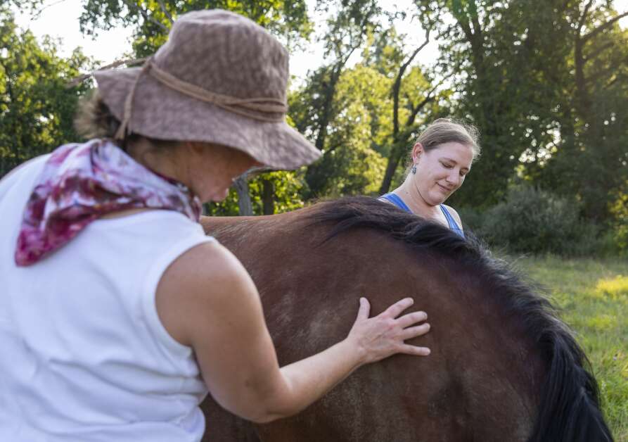 Freyja Stoltz of Iowa City, left, and Anna Evans of Iowa City pet one of the mares as it grazes in a pasture during The Well Lived Life retreat at Lovely Bunches Farm in Iowa City, Iowa on Sunday, August 20, 2023. (Savannah Blake/The Gazette)