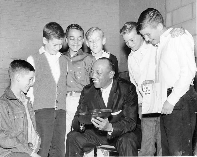 Jesse Owens, Olympic gold medalist and a youth sports instructor, talks  with boys at the Cedar Rapids YMCA in May 1960. Owens is holding one of the awards presented that night, while a boy on the far right holds a program from the banquet. The boys are not identified in the photo. (Gazette archives) 