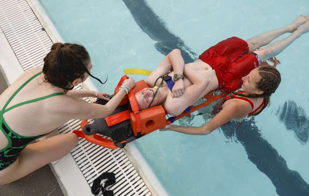 Sheppard West, 16, is strapped to a backboard by Maddie Esno (left), 16, and Kortney Travis, 17, as they practice water rescues during lifeguard training May 17 at Cherry Hill Aquatic Center in northwest Cedar Rapids. (Jim Slosiarek/The Gazette)