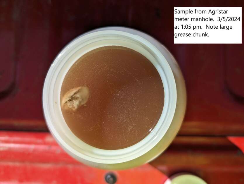 A sample of wastewater from Agri Star, a Postville meat processor, is tinted red and has a floating grease chunk. A blocked sewer line at Agri Star caused a pump station to flood, sending untreated water from a beef kill facility to the Postville city treatment plant. (City of Postville)