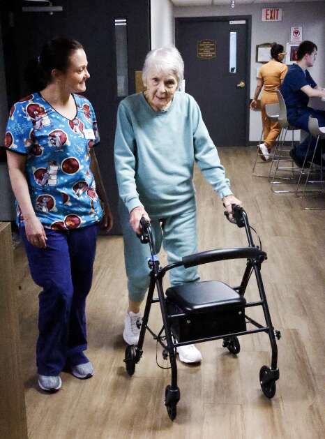 Cassy McSpadden (left) walks with resident Eleanor Arp at West Ridge Care Center in northwest Cedar Rapids on May 8. McSpadden is a Certified Nursing Assistant (CNA) and an Oral Medication Technician (OMT). She’s been at the facility since 2003.   (Jim Slosiarek/The Gazette)