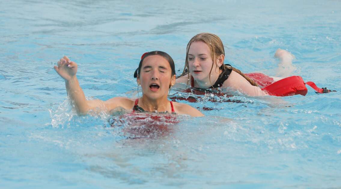 Ella Dolan, 16, (right) swims up behind Alyza Koppes as Koppes plays the victim during an active drowning water rescue exercise during lifeguard training at Cherry Hill Aquatic Center in northwest Cedar Rapids, Iowa, on Wednesday, May 17, 2023. Pools in the Corridor will open for the season this Memorial Day weekend.  (Jim Slosiarek/The Gazette)