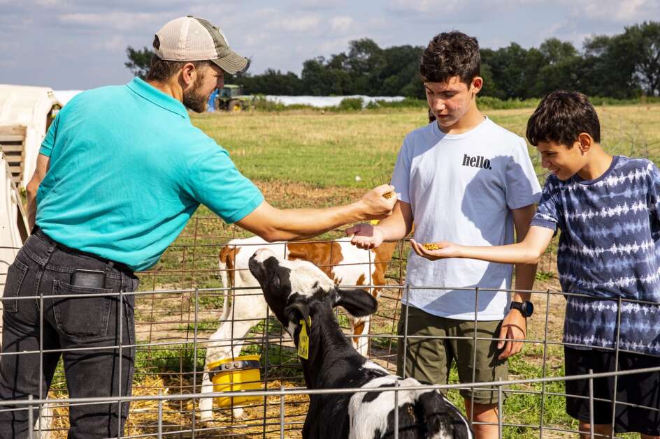 Dan Bolin hands some cattle feed to Ian and Aric Eason on Aug. 17 at New Day Dairy in Clarksville. (Nick Rohlman/The Gazette)