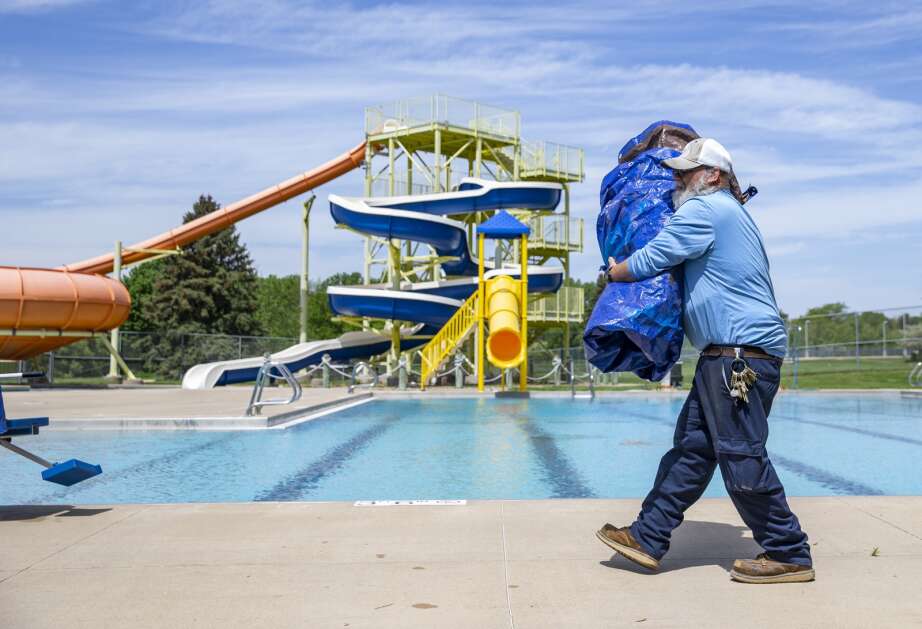 City worker Kevin Wise carries a tarp to storage after uncovering the pool May 16 at the Coralville Community Aquatic Center. The pool will open at noon June 3. (Savannah Blake/The Gazette)
