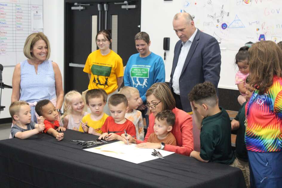 Iowa Gov. Kim Reynolds, flanked by staff, children and state lawmakers, signs into law legislation that expands eligibility in the state's child care assistance program for low-income residents during a May 18 ceremony at ChildCare Discovery Center in Fort Dodge. (Erin Murphy/Gazette Des Moines Bureau) 