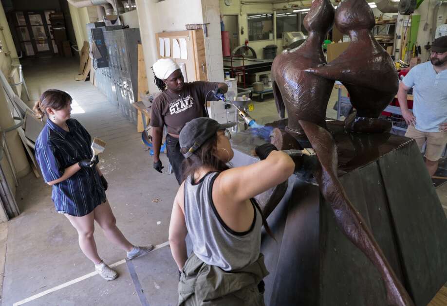 Clockwise from left: University of Northern Iowa junior Stacia Iverson, senior Sarah Byrd and recent graduate Amelia Gotera take turns using a torch June 26 to heat the surface of the sculpture “Between Friends” and applying wax as the sculpture undergoes a refurbishment on the Cedar Falls campus. (Jim Slosiarek/The Gazette)