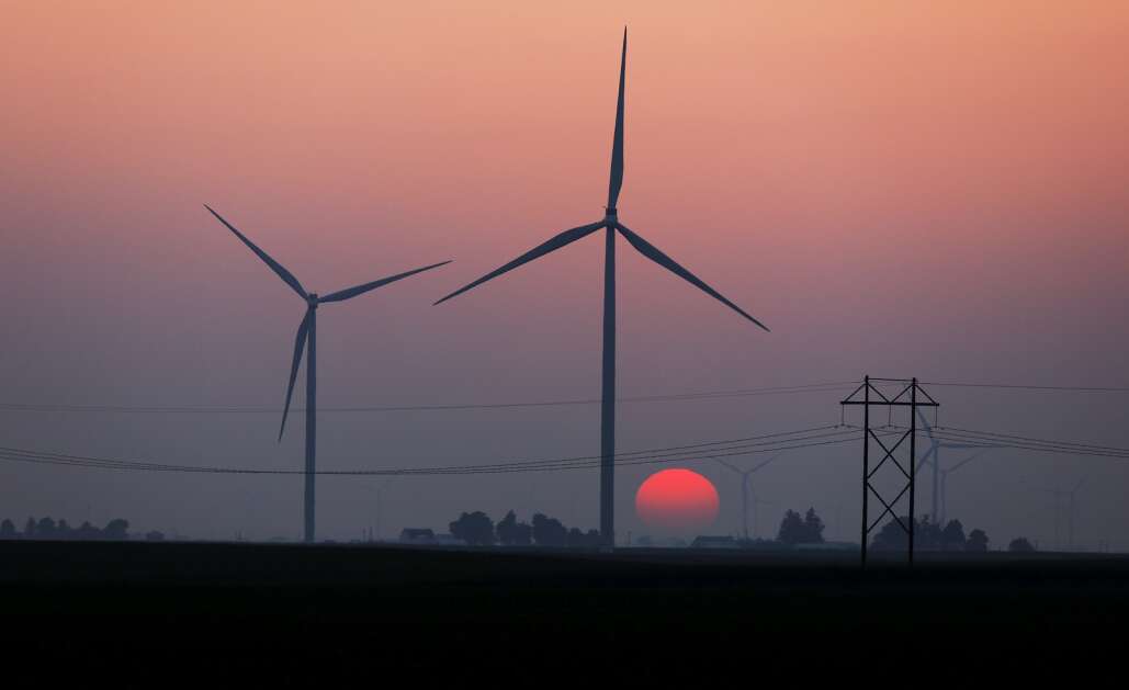 The Sun sets as wind turbines generate electricity near Montezuma in rural Poweshiek County on July 20, 2022.  Both Alliant Energy and MidAmerican Energy operate wind farms near each other in the county. A new analysis by Brown University shows the power of lobbyists, including those for utilities, in affecting energy-related legislation in Iowa. (Jim Slosiarek/The Gazette)
