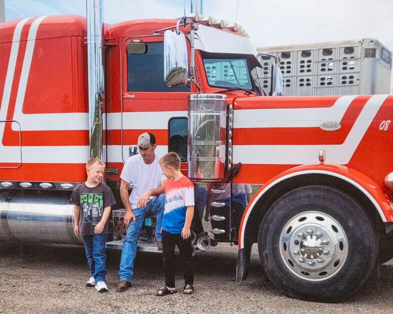David Schultz is pictured with his twin sons Joseph (left) and Isaack next to his Peterbilt semi-truck. His wife Sarah's name is painted on the passenger door. (Provided photo)