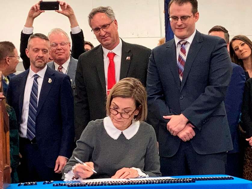 Iowa Gov. Kim Reynolds, flanked by Lt. Gov. Adam Gregg, right, and Iowa lawmakers, signs a tax reform bill into law that creates a flat tax, cuts retirement income taxes and reduces corporate taxes, on March 1, 2022, in Des Moines, Iowa. (AP Photo/David Pitt)