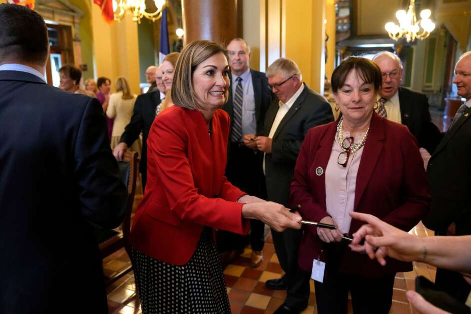 Iowa Gov. Kim Reynolds passes out pens Thursday after signing a property tax cut bill at the Statehouse in Des Moines. She told reporters she would soon sign a bill that eases restrictions on employing children. (AP Photo/Charlie Neibergall)
