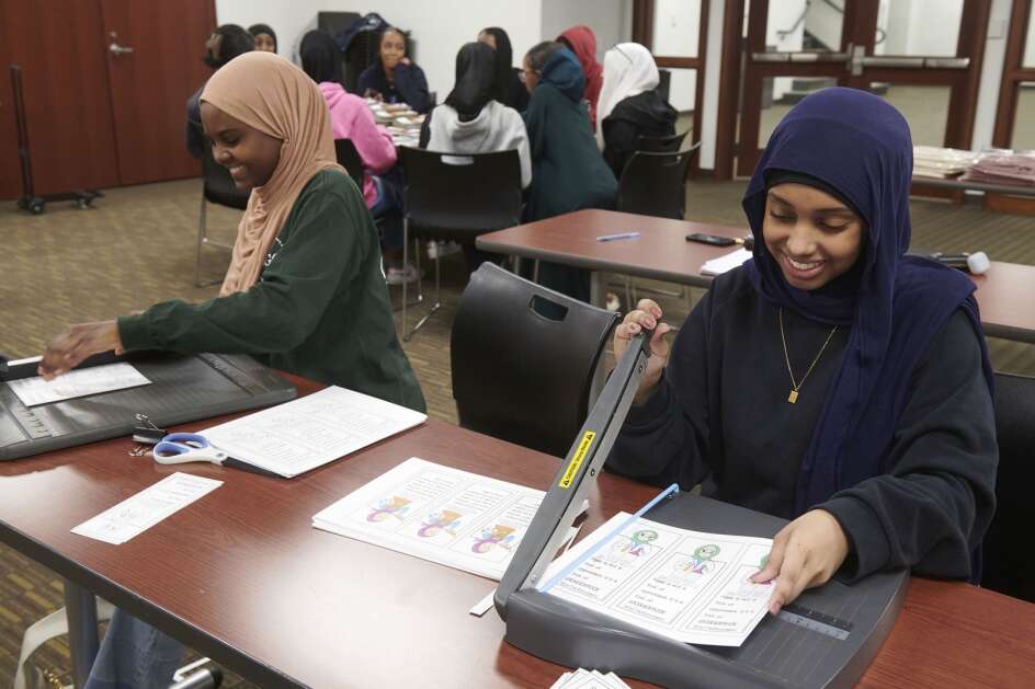 (from left) Omnia Ahmed, age 16 of Iowa City, and Zaina Mohamed, age 16 of North Liberty, trim bookmarks as members of the Mariam Girls’ Club prepare for an upcoming annual World Hijab Day event at the Coralville Public Library on Saturday, January 27, 2024. The club is partnering for the second year with the library to host a public World Hijab Day event on Thursday, February 1 at 4:30pm where participants can learn about the hijab and women in Islam. “We are organizing this event to bring awareness, to foster personal freedom of religious expressions, and to dismantle bigotry, discrimination, and prejudice against Muslim women and girls wearing the hijab” says Viana Qadoura, founder and director of the Mariam Girls Club, a group that offers young Muslim women an empowering and safe space in the Iowa City area. (Cliff Jette/Freelance)