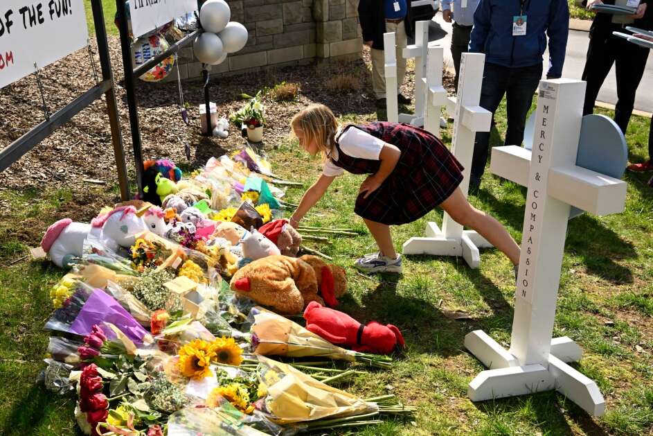 A young girl places an item at a growing memorial,Tuesday, March 28, 2023, in Nashville, at an entry to Covenant School for the victims of Monday' shooting. (AP Photo/John Amis)
