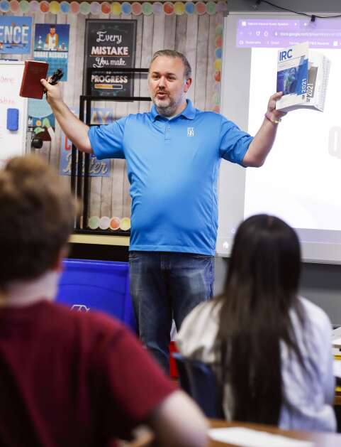 Linn County associate combination building inspector Ryan Sampica holds up a 1925 Cedar Rapids, Iowa, Building Code book (left) and a 2021 International Residential Code book for one- and two-family dwellings as he gives a presentation on building codes, building practices and how they relate to natural disasters to Valerie Sampica's sixth grade class at Roosevelt Creative Corridor Business Academy in southwest Cedar Rapids, Iowa, on Friday, May 12, 2023. (Jim Slosiarek/The Gazette)