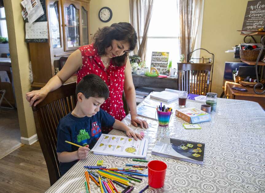 Gabriella Rustebakke check over 7-year-old Paul Rustebakke’s math worksheet during an April 13 math lesson at their home in Cedar Rapids. (Savannah Blake/The Gazette)