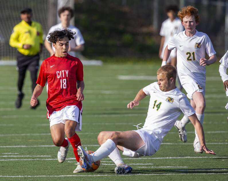 Kennedy Cougars defender Trevor Shanle (14) slides to knock the ball away from City High Little Hawks midfielder Josh Borger-Germann (18) as he dribbles the ball down the field in the second half of the game at Iowa City High in Iowa City, Iowa on Tuesday, April 25, 2023. (Savannah Blake/The Gazette)