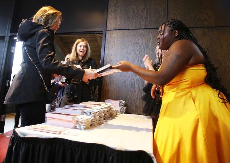 Public relations and marketing Director Bria Felix hands out a copy of Steve Madden's memoir to a guest April 15 at The Fashion Show at Stephens Auditorium in Ames. (Bailey Cichon/The Gazette)