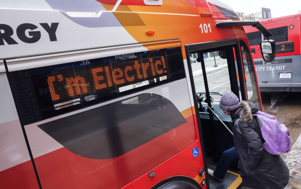 A passenger gets on an electric bus Jan. 27, 2022, as a sign announces that it's electric outside Old Capitol Town Center in Iowa City. (Jim Slosiarek/The Gazette)