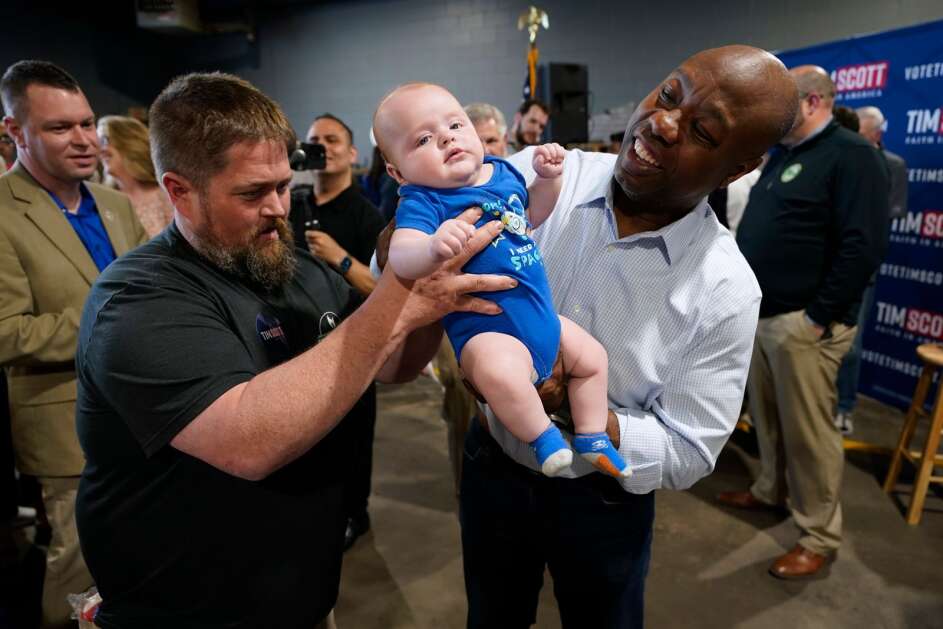 Republican presidential candidate Sen. Tim Scott of South Carolina holds 3-month-old Sawyer Thompson, of Council Bluffs, as his father, Jeff, looks on during a town hall meeting Wednesday in Sioux City. (Charlie Neibergall/Associated Press) 