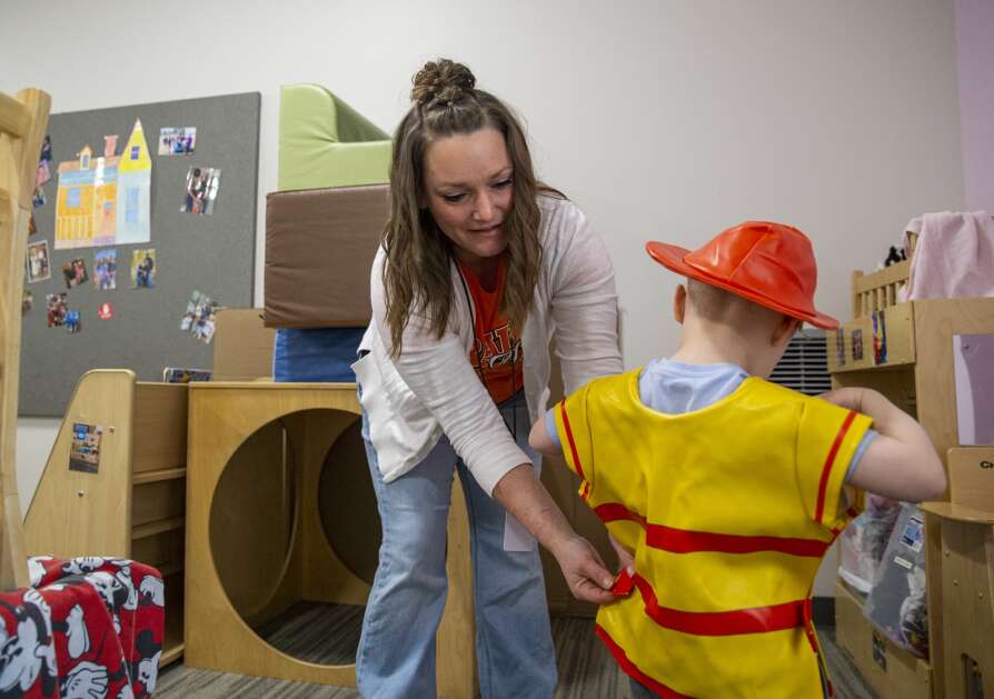 Ashley Barr helps a child put on a firefighter costume during play time Friday at the Prairie Early Childhood Center in Cedar Rapids. The College Community School District helped Barr and her two children when they faced homelessness. (Savannah Blake/The Gazette)