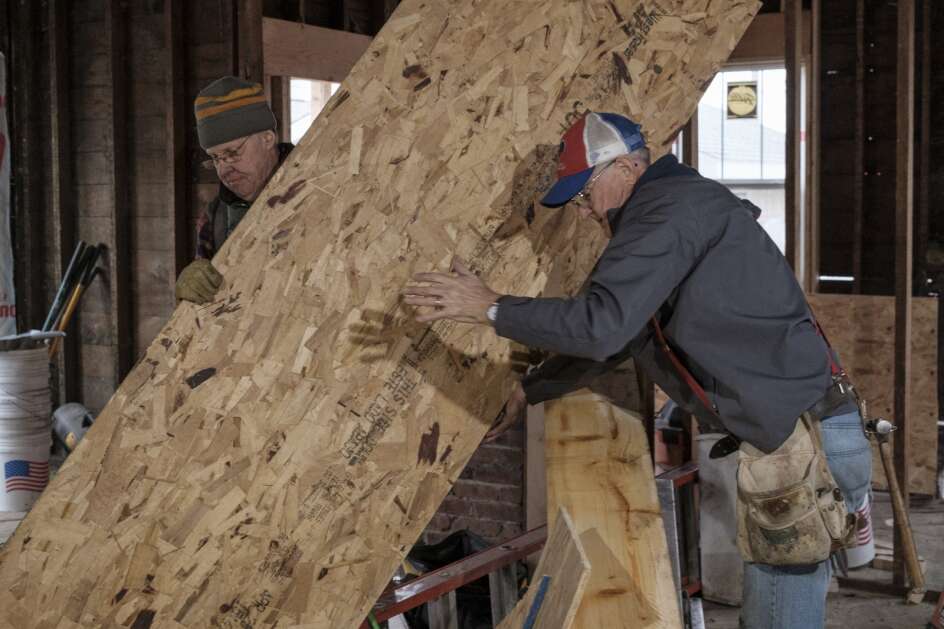 John McCormick (left) and Mick Rosenau move a piece of plywood April 1 at a home being restored by Iowa Heartland Habitat for Humanity in the Church Row neighborhood in Waterloo. (Nick Rohlman/The Gazette)