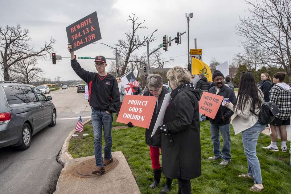 Protest organizer Gage West (left) holds a sign during a protest against the Linn-Mar school board’s passage of policies to protect transgender students from discrimination near Linn-Mar High School in Marion, Iowa on Friday, May 6, 2022. West Graduated from Linn-Mar High School in 2019. (Nick Rohlman/The Gazette)