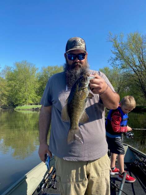 Sam Patterson of Atkins poses with a husky smallmouth bass while his 7-year-old son River fishes in the background. (Orlan Love/correspondent_