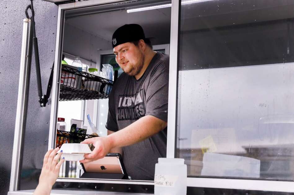 Nicholas Fitzgerald hands a food order to a customer at Smiley's food truck in the Lindale Mall parking lot in northeast Cedar Rapids in May 2021. Smiley’s previously participated in the Food Truck Tuesdays at NewBo City Market, which will be returning for its fifth year in May. (Jim Slosiarek/The Gazette)