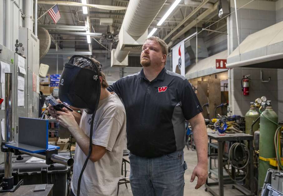 Kevin Wilkinson, an industrial technology teacher,  helps senior William Van Dee get started on the virtual welding machine May 9 at Williamsburg High School in Williamsburg. The machine allows students to practice welding techniques before using a gas- powered welder. (Savannah Blake/The Gazette)