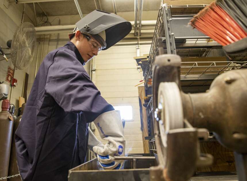 High school junior Christopher Yenter cools welded pieces of metal in a bucket of water after completing a live weld May 9 at Williamsburg High School. Yenter will be a welding apprentice at Kinze Manufacturing in Williamsburg this summer. (Savannah Blake/The Gazette)